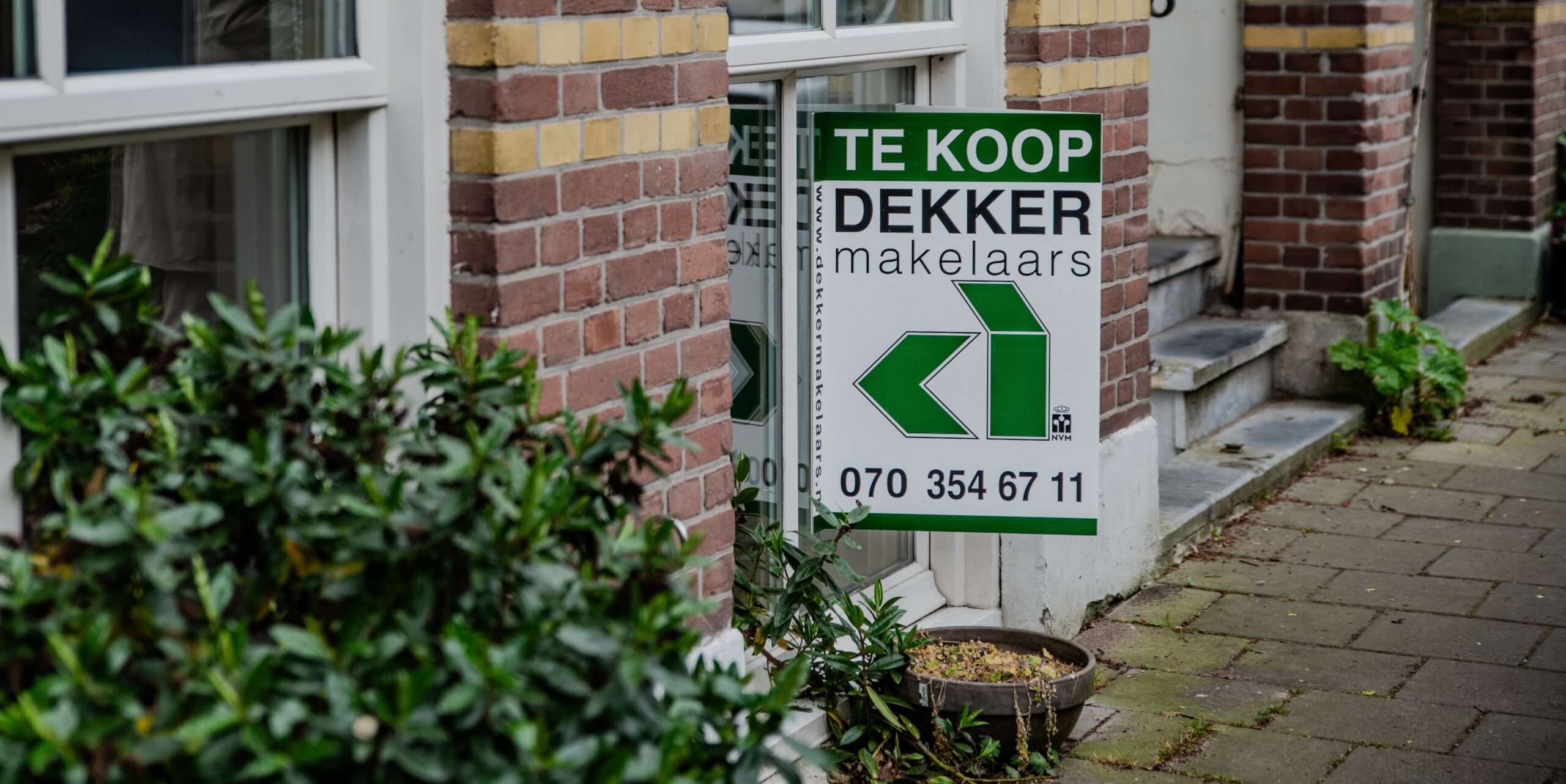 Een hangend Te Koop-bord van Dekker Makelaars - Zoekopdracht - Dekker Makelaars - Makelaar Den Haag